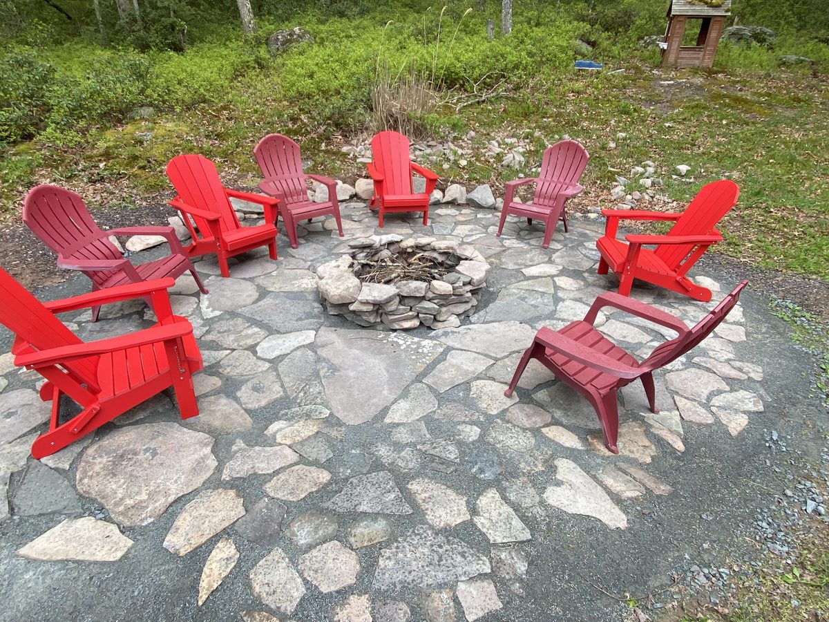 Stone fire pit ringed with red Adirondack chairs